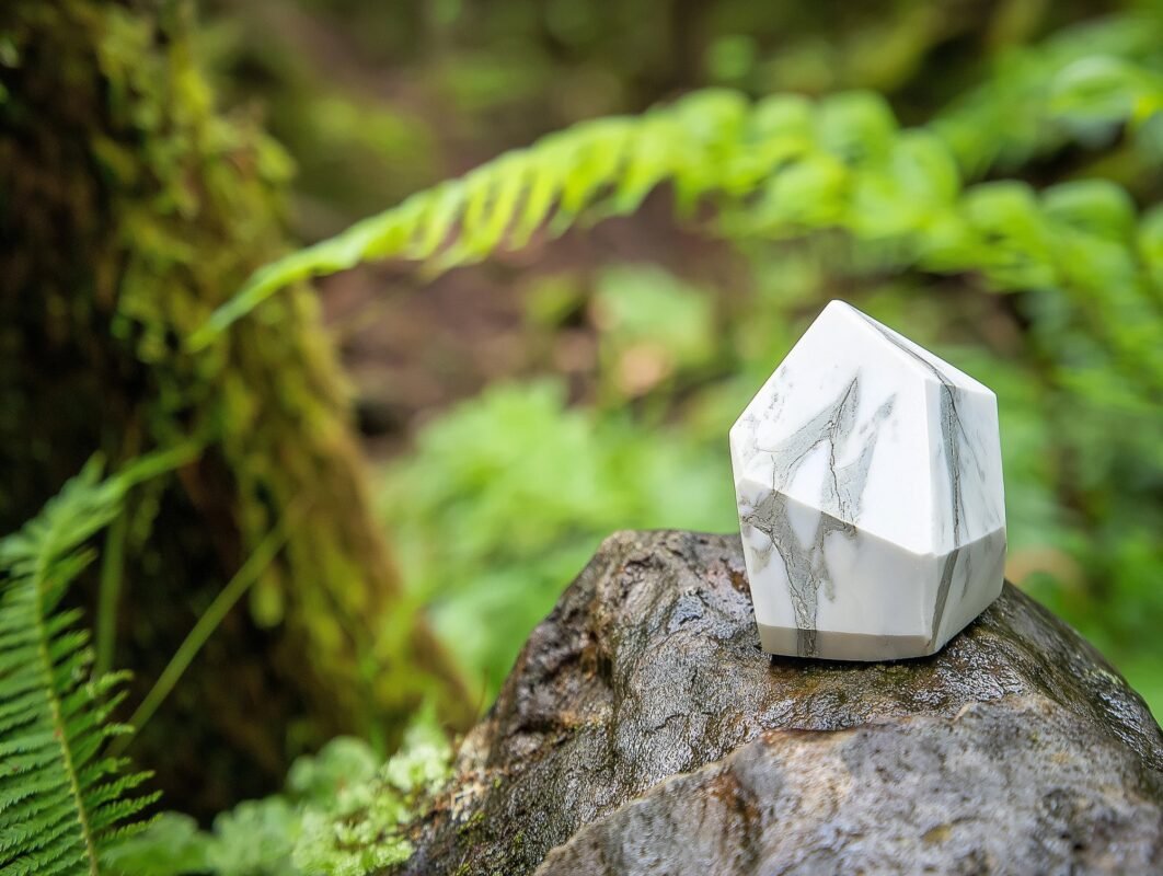 Close up view of a raw white howlite stone resting on a textured rock surface in an outdoor natural setting. – Terralith